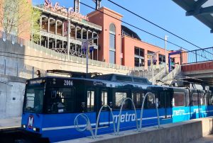 MetroLink train stopped at the platform of the Stadium MetroLink station. Busch Stadium is showing in the background.
